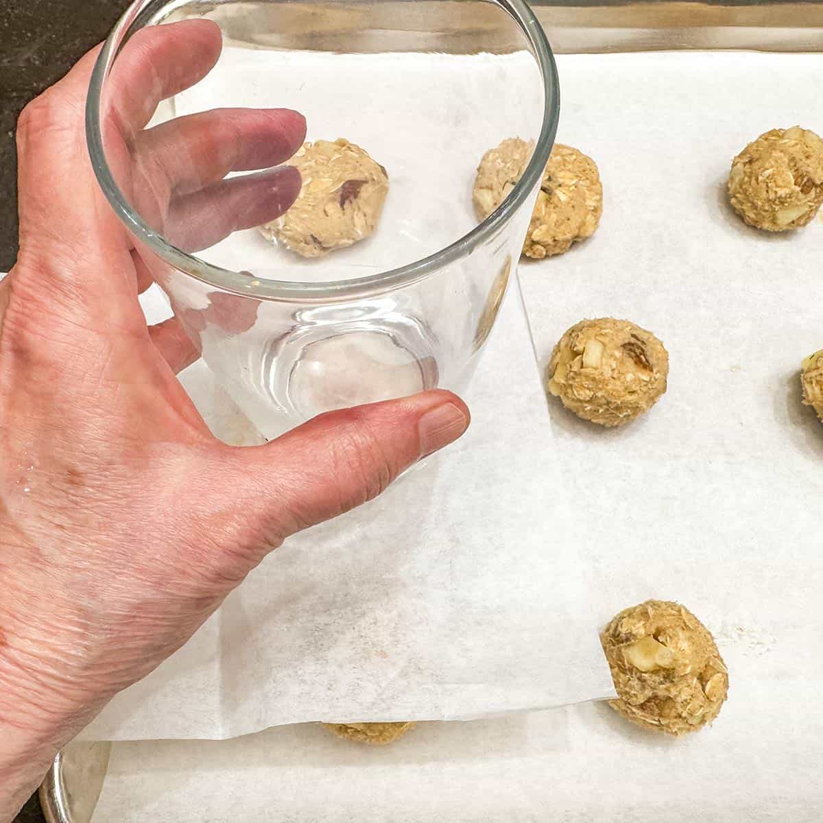 Using a flat bottom glass with a piece of parchment paper between the glass and the scooped cookie ball to flatten.