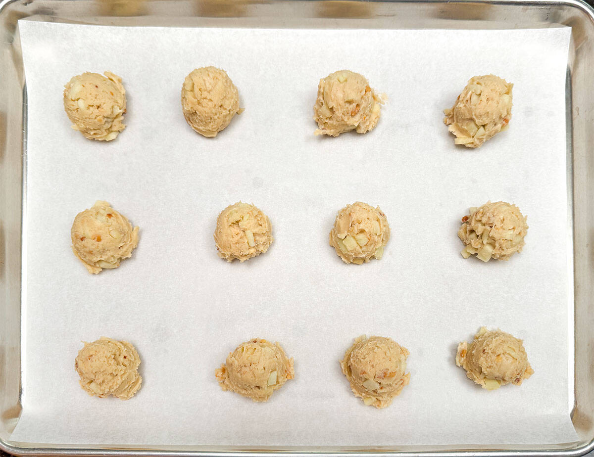 Twelve scooped cookie balls on a parchment paper lined sheet pan.