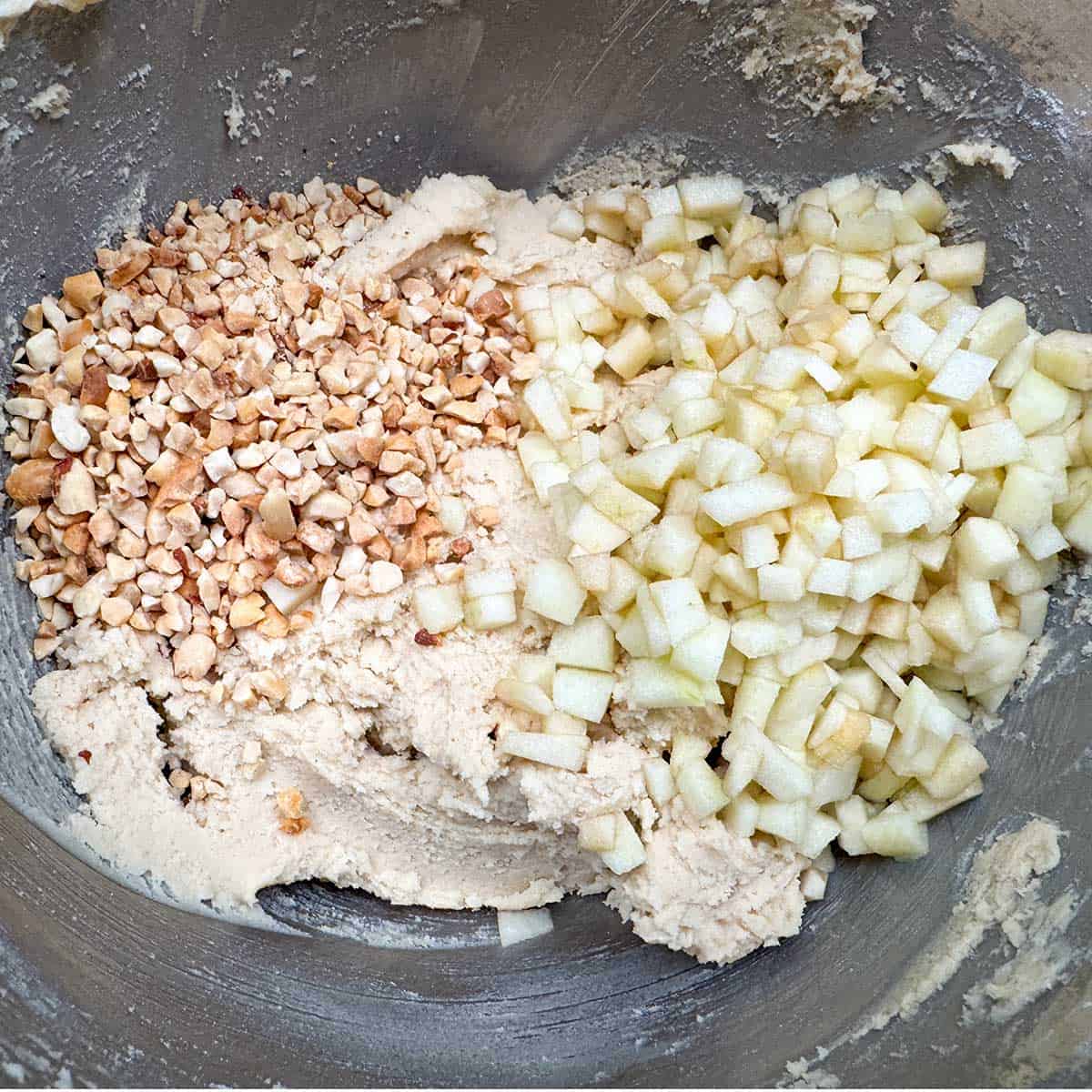 Adding chopped peanuts and diced apples to the cookie dough in the mixer bowl.