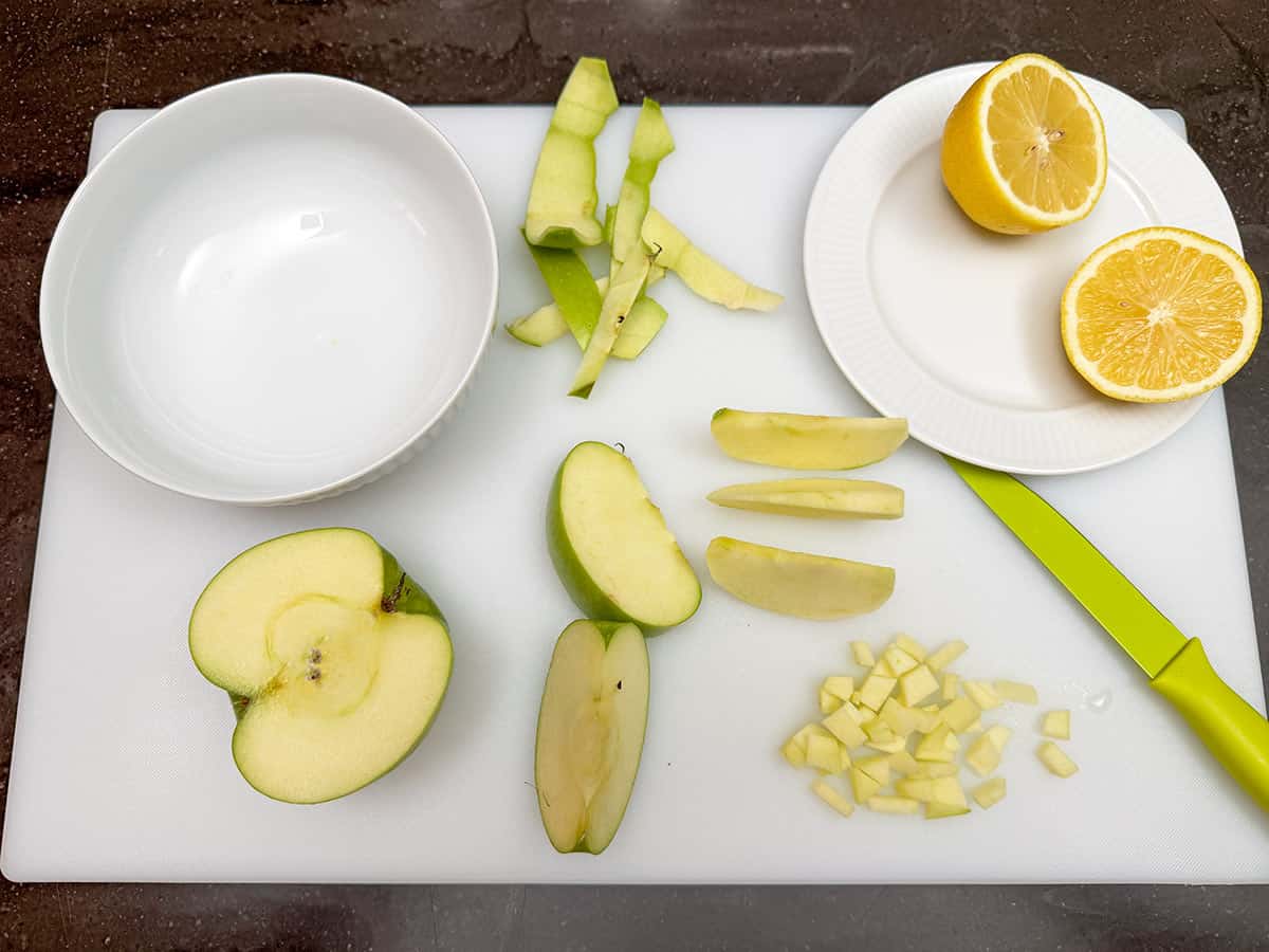 Dicing an apple on a cutting board with a lemon cut in half to sprinkle on the cut apple so they do not turn brown.