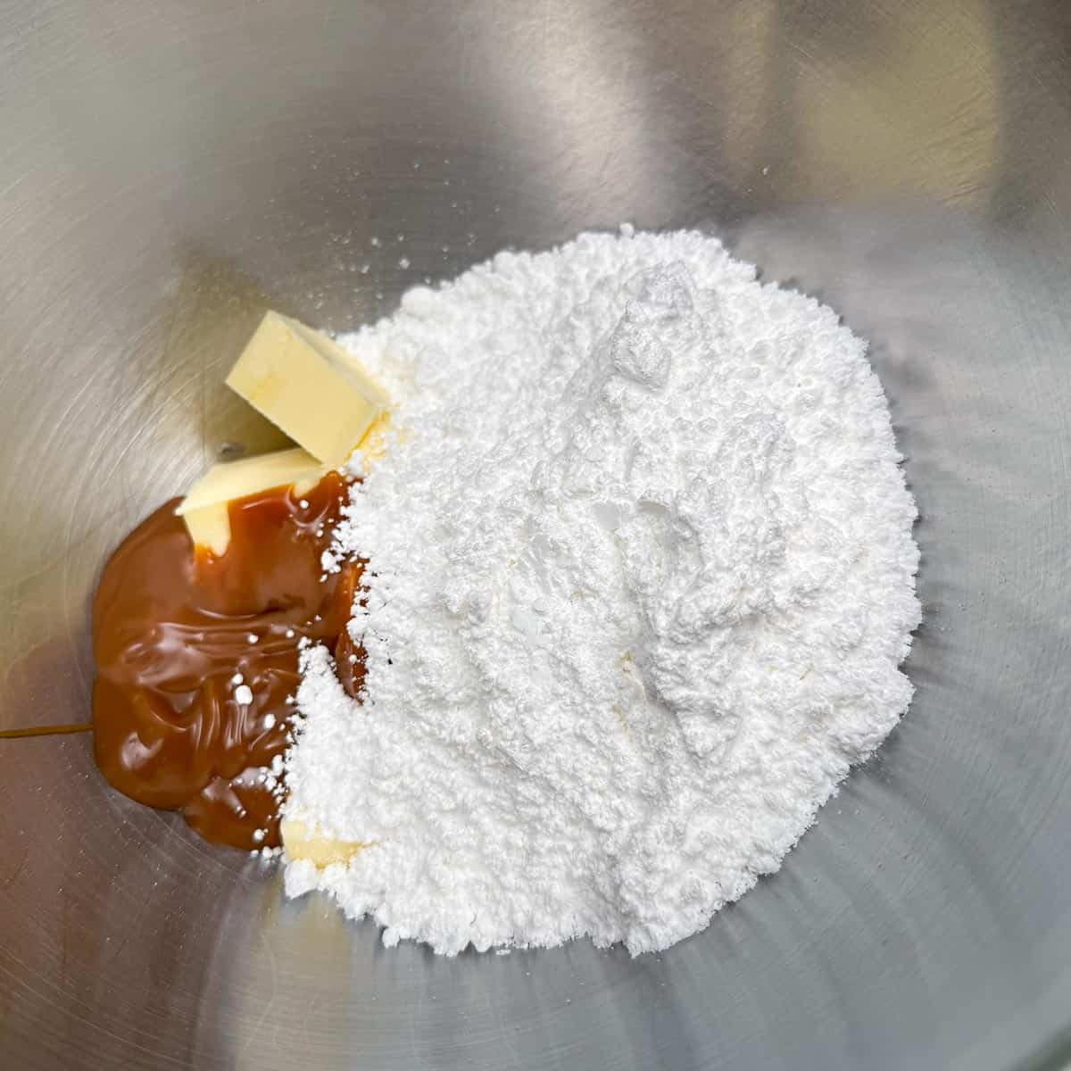 Adding butter, caramel dip, and powdered sugar to a mixer to be mixed into frosting.