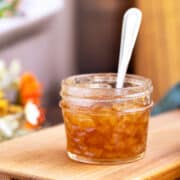 Homemade pear filling in a jar sitting on wooden cutting boards with a spoon in the jar.