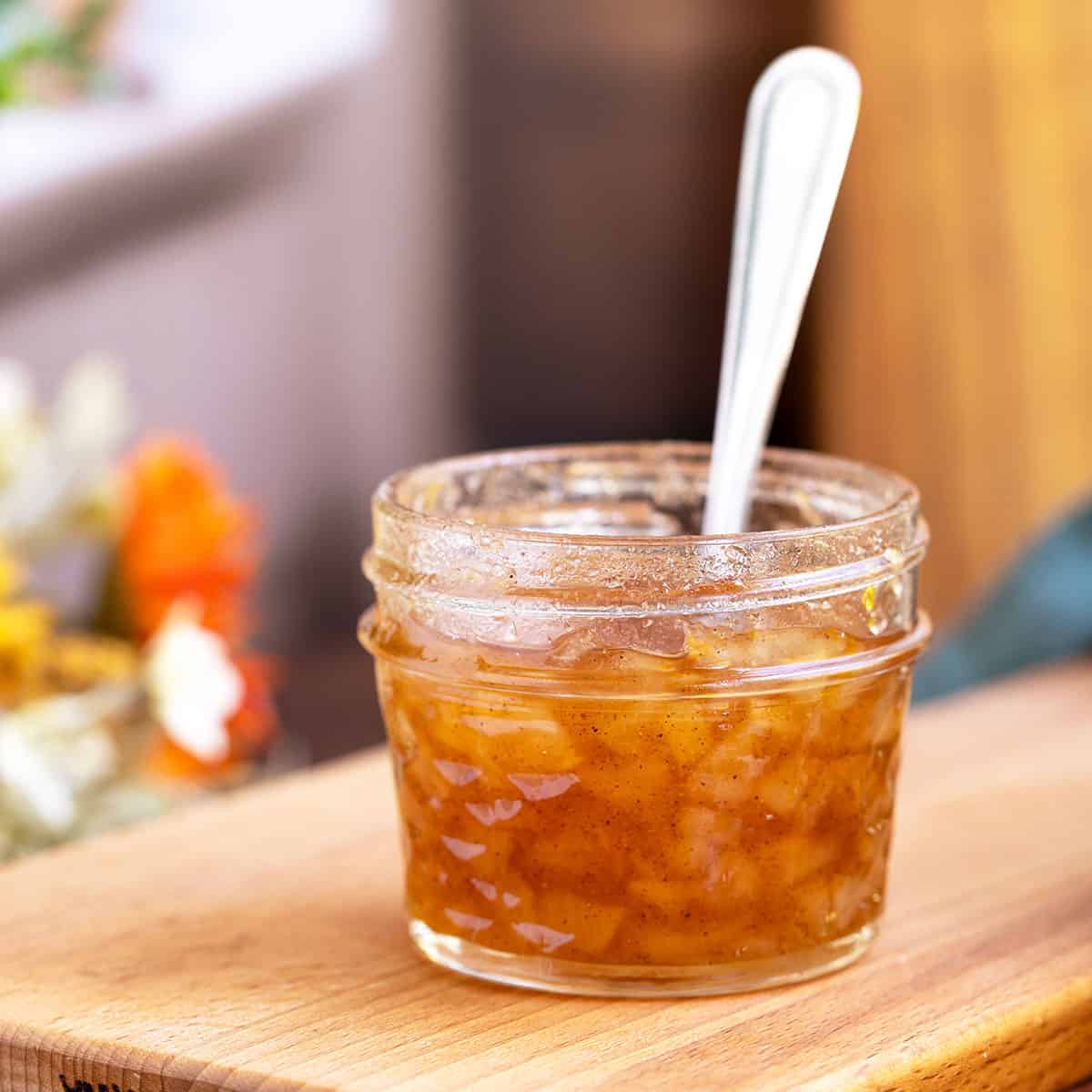 Homemade pear filling in a jar sitting on wooden cutting boards with a spoon in the jar.