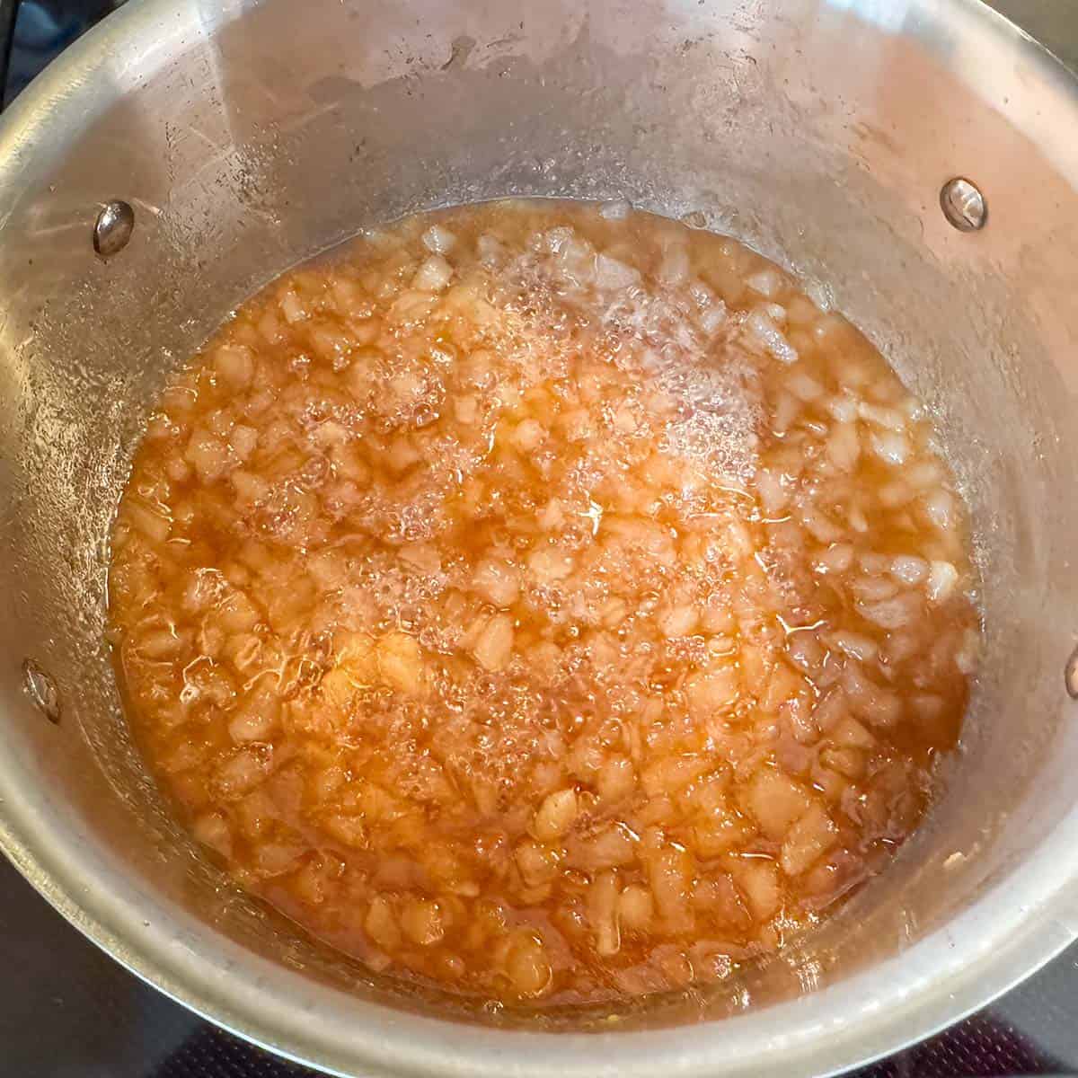 The pear filling in the saucepan takes on a darker color as the liquid is reduced.