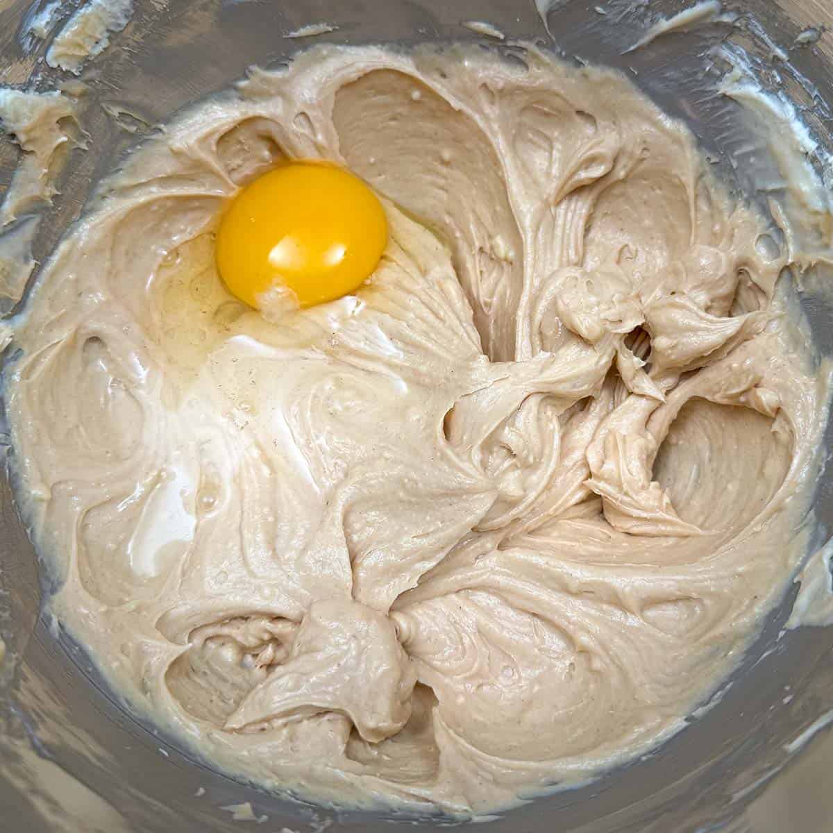 Adding an egg to the wet cookie dough in the mixer bowl.