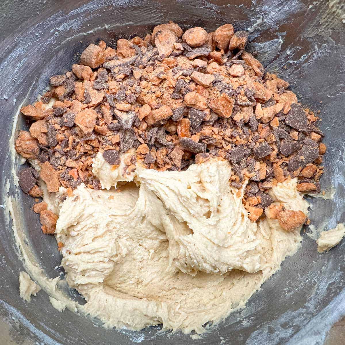 Putting the Butterfinger bits into the mixer bowl on top of the cookie dough.