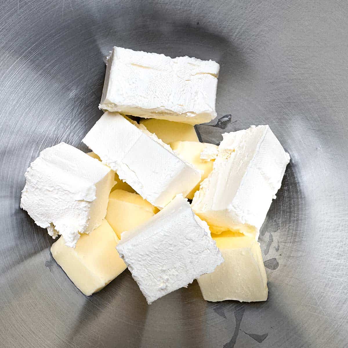 Adding cubed butter and cream cheese blocks into a mixer bowl.