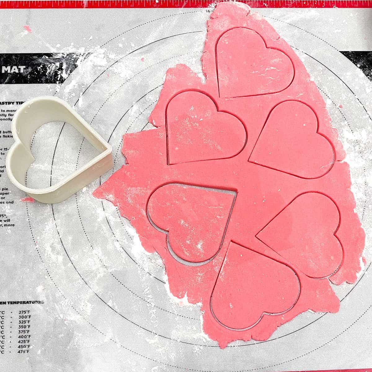 Heart cutter cutting out the cookies to be placed on the sheet pan to bake.