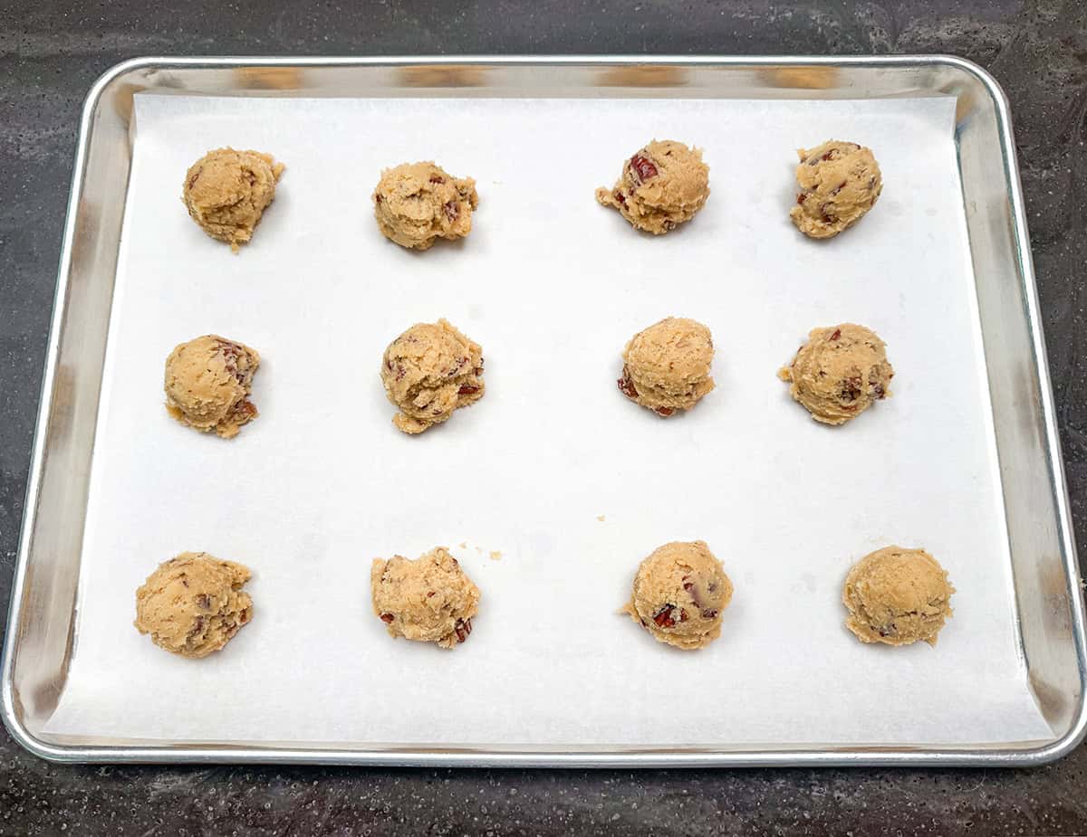 Twelve scoops of cookie dough on a parchment-lined sheet pan.