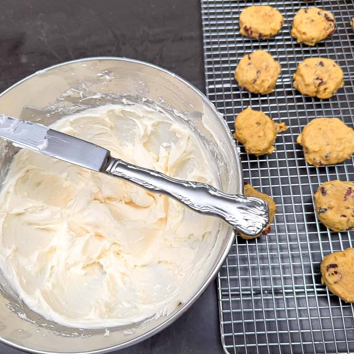 Icing in a mixer bowl with a knife laid across the top to the bowl ready to put icing on the baked cookies.