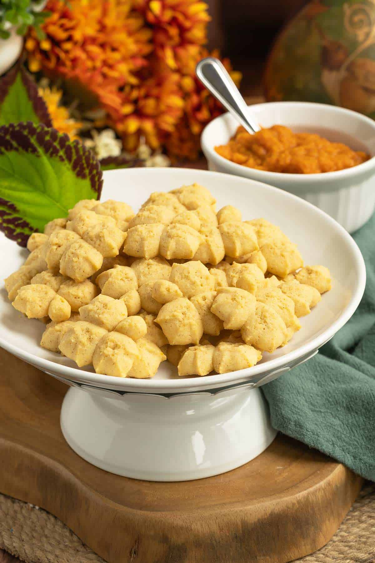 A plate full of finished Pumpkin Pie Spritz Cookies with a small bowl of pumpkin puree.