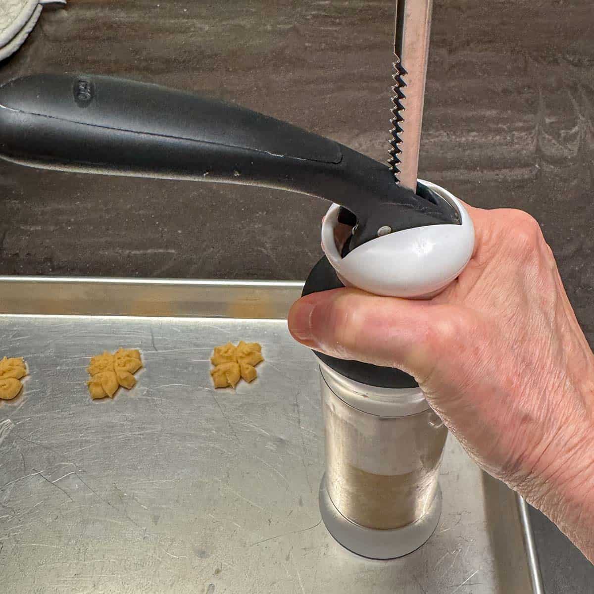Holding the filled cookie press against the sheet pan to press out the cookie dough.